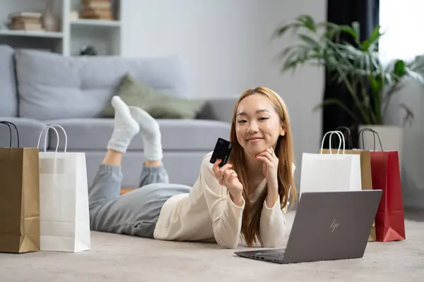 Young Woman Enjoying Online Shopping Lying Laptop Credit Card Casual lizenzfreie Stockfotos