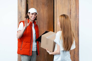 Dost canlısı teslimatçı paket teslim ederken müşteriye el sallıyor. Ev teslimatı, çevrimiçi alışveriş ve müşteri memnuniyeti konuları için mükemmel..