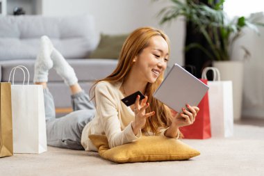 Çevrimiçi alışveriş yapan mutlu genç kadın elinde kredi kartı ve tablet ile gülümsüyor. Konforlu E-ticaret Deneyimi.