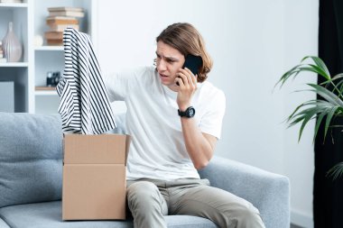 Çevrimiçi alışveriş teslimatı ile hayal kırıklığına uğrayan genç adam, telefonla konuşurken yanlış nesne alıyor, Modern Oturma Odası Arka planı