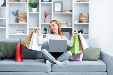İnternetten alışveriş yapan mutlu genç kadın dizüstü bilgisayarlı gülümseyen Asyalı kadın ve renkli alışveriş torbaları, e-ticaret anlayışı.