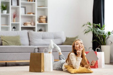 Alışveriş torbaları evde dinlenen, online alışveriş başarısının keyfini çıkaran, modern apartmanda sıradan bir yaşam tarzı olan mutlu genç kadın.