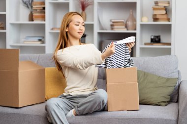 Yeni Apartman 'da kutuları açan genç bir kadın hoşnutluk dolu kıyafetlere bakıyor. Taşınmanın, yeni başlangıçların ve ev hayatının temaları için mükemmel..