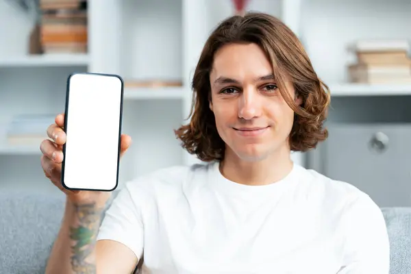 Smiling Young Man White Shirt Showing Blank Smartphone Screen Indoors รูปภาพสต็อกที่ปลอดค่าลิขสิทธิ์