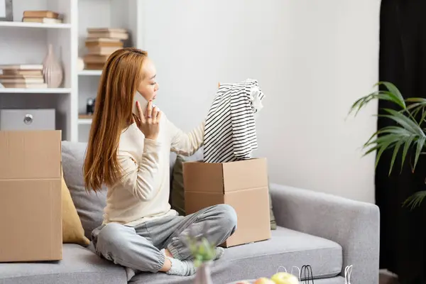 Young Woman Unpacking Clothes Feeling Joyful Relaxed While Sitting Sofa Stockfoto