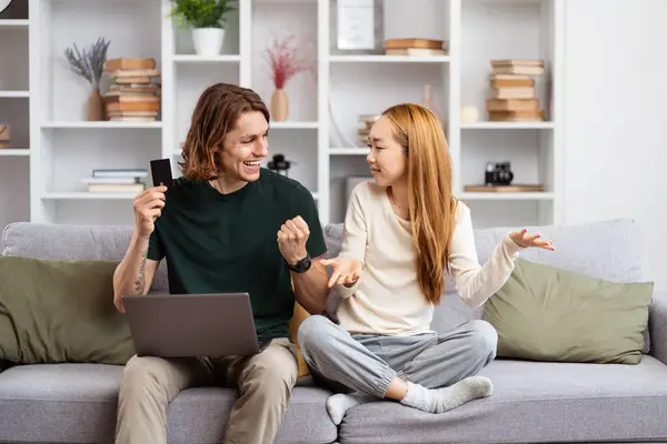 Young Couple Enjoying Lively Conversation Couch Man Holding Credit Card Stockfoto
