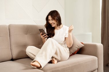 Oturma Odasında Akıllı Telefonun Başarısını Kutlayan Kadın: Mutlu, Heyecanlı, Ev İçi, Sıradan Yaşam Tarzı