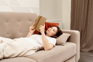 Rahat kadın koltukta kitap okuyor, rahat ev içi, boş zaman, rahat oturma odası sahnesi.