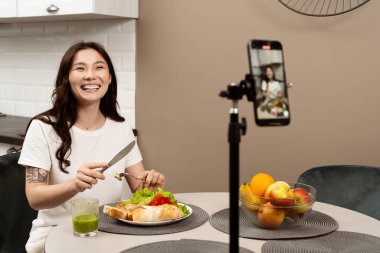 Neşeli Genç Kadın Modern Mutfakta Akıllı Telefonla Sağlıklı Yemek Hazırlama 'yı çekiyor. Günlük, Yaşam Tarzı, Yemek Blogu