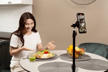 Gıda Blogcusu İçerik Oluşturucu: Neşeli genç bir kadın, modern bir mutfakta sağlıklı yemek, açık büfe yemekleri, yaşam tarzı blogları ve dijital içerik oluşturma videolarını kaydediyor.