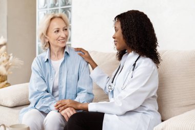Doktor, ev ziyareti sırasında yaşlı kadını rahatlatıyor, güven ve şefkat dolu sağlık hizmetleri gösteriyor.