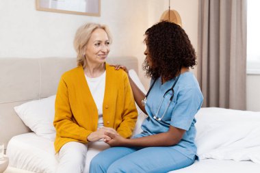 Hastane odasında yaşlı bir kadını rahatlatan hemşire. Sağlık personeli bakım ve destek sağlıyor. Sağlık hizmetleri. Merhametli Hemşirelik ve Hasta Etkileşimi. Bakım Ortamı ve Profesyonel Yardım.