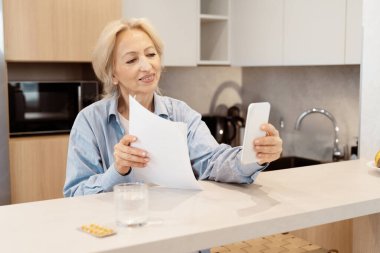 Modern Mutfakta Üst Düzey Kadın Evrakları Kontrol Ediyor ve Akıllı Telefon Kullanıyor
