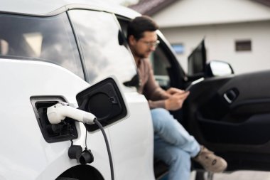 İnsanlar Akıllı Telefon, Çevre dostu Ulaşım ve Teknoloji Konsepti Kullanırken Elektrikli Araç Şarjı.