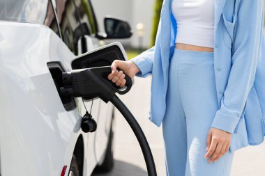 Kadın elektrikli arabayı şarj kablosuyla şarj ediyor.