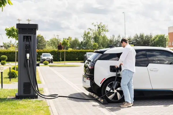 stock image Man Charging Electric Car At Station In Urban Area, Clean Energy And Eco-Friendly Transportation Concept