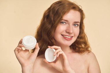 Cilt kremi kavanozu tutan, gülümseyen ve ürünleri gösteren kadın. Doğal Güzellik, Cilt Rutini ve Kişisel Bakım