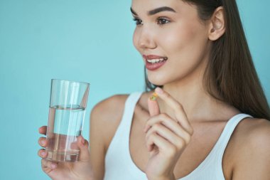 Diyet, elinde bir bardak su ve açık mavi arka planda vitamin hapı tutan kadın. Sağlık, sağlık ve günlük destek kavramı.. 