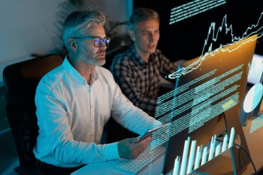 Büyük bilgisayar ekranlarındaki verileri analiz eden, finansal tablolar ve grafiklere odaklanan iş adamları. Ofis ortamında işbirliği yapan iki adam, Takım Çalışması, Teknoloji