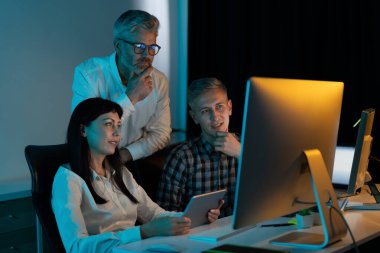 Ofisteki bilgisayar projesinde işbirliği yapan profesyonellerden oluşan bir ekip fikir alışverişi yapıyor ve stratejiyi tartışıyorlar. Modern Çalışma Ortamı ve Teknolojisi, Takım Çalışması, İşbirliği, İş Planlama