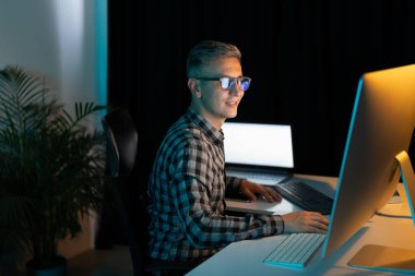 Bilgisayarda geç saatlere kadar çalışan, ofiste dizüstü bilgisayar kullanan, kendini işine adamış, modern çalışma alanında gece vardiyasında çalışan bir adam.