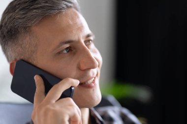 Akıllı telefondan konuşan, gülümseyen, sohbet eden bir adam. Yakın çekim Duygular, İletişim, Bağlantı, Teknoloji ve İş Etkileşimi.