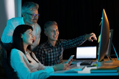 Modern Ofiste bilgisayar projesinde işbirliği yapan, gülümseyen ve meşgul olan, takım çalışmasını, teknolojiyi ve yeniliği vurgulayan üç profesyonel.