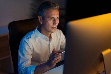 Ofiste geç saatlere kadar bilgisayar başında çalışan, görevine odaklanmış, kendini adamış ve verimlilik kavramına odaklanmış bir adam.