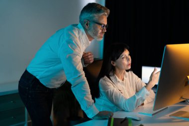 Gece geç saatlerde ofiste işbirliği yapan birimler bilgisayar ekranı, profesyonel takım çalışması ve iş stratejisine odaklanmış durumdalar.