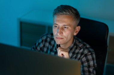 Ofiste geç saatlere kadar bilgisayar başında çalışan, odaklanan, kararlı ve düşünceli bir adam.