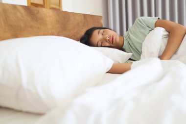 Yatakta uyuyan huzurlu bir kadın, yumuşak beyaz yastıklar ve rahat battaniye, rahatlık ve sükunet, yatak odasında mükemmel uyku ortamı, sükunet ve sükunet ile çevrili bir şekilde dinleniyor.
