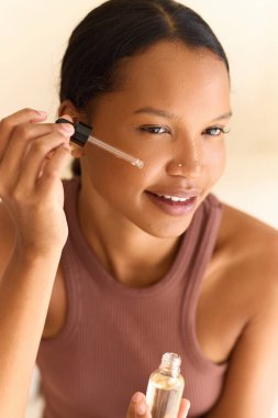 Bir kadın kendinden emin bir şekilde yüz serumu uyguluyor, cilt bakımını ve kendine bakım rutinlerini vurguluyor. Yakın plan, sağlıklı ve ışıl ışıl bir teni vurgulayan kişisel sağlık ve güzellik anı yakalıyor..