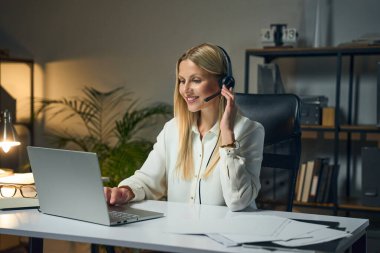 İç İşleri Bakanlığı 'ndan görüntülü arama yapan gülümseyen kadın, profesyonel çalışma alanı atmosferinde dizüstü bilgisayarlar, kağıtlar ve kapalı santral ile modern teknolojiyi temsil ediyor..