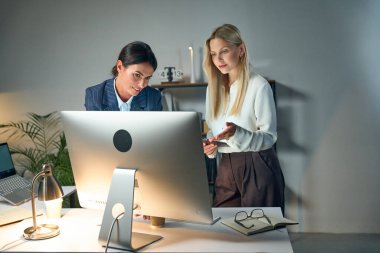 Modern bir ofis ortamında bilgisayar üzerinde işbirliği yapan, takım çalışması, verimlilik ve kurumsal bir ortama odaklanan iki profesyonel kadın..