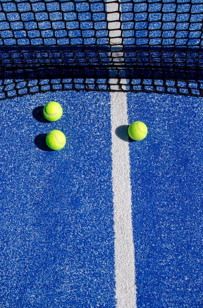 Mavi bir tenis kortunda, ağın yanında üç top.