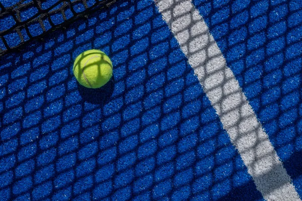Mavi raket tenis kortunun gölgesi topun üzerine düşüyor.