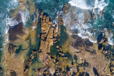 Deniz dalgalarının kayalık bir sahile vuruşunun üst görüntüsü.