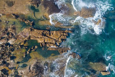 Deniz dalgalarının yukarıdaki görüntüsü kayalık bir sahile çarpıyor.