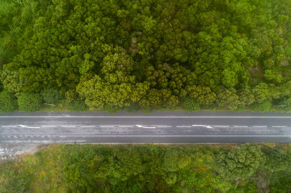 Aerial top view of asphalt road through green forest