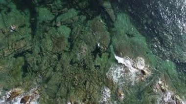 Denizin şeffaf yeşil sularının üzerinde insansız hava aracıyla kayalık bir sahilde yükselen görüntüler.