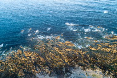 Güneşin doğuşunda kayalık bir plajın zenital hava manzarası