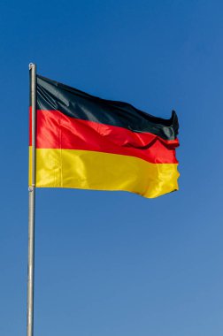 Mavi gökyüzünde rüzgarda dalgalanan Alman bayrağı
