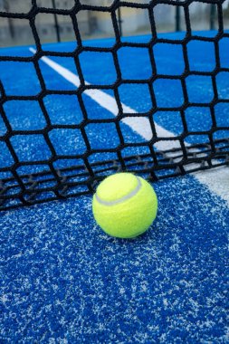 Açık havada mavi kortta kürek ağının önünde sarı top. Padel tenis kortu