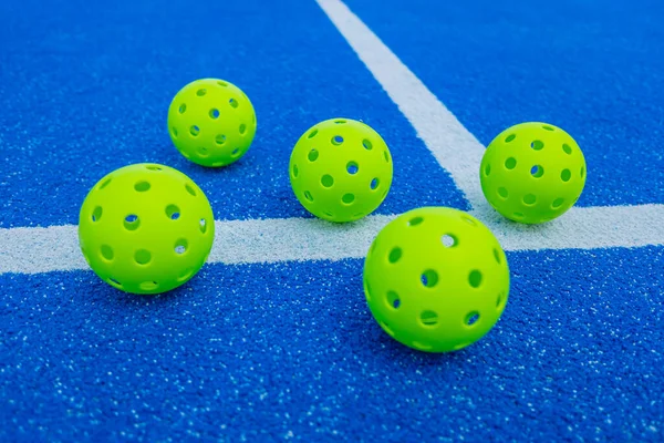 Mavi bir saha çizgisinin yanında beş tane picleball topu, raket sporu konsepti.