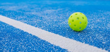 Pickleball topu mavi bir picleball sahasına yakın, afiş