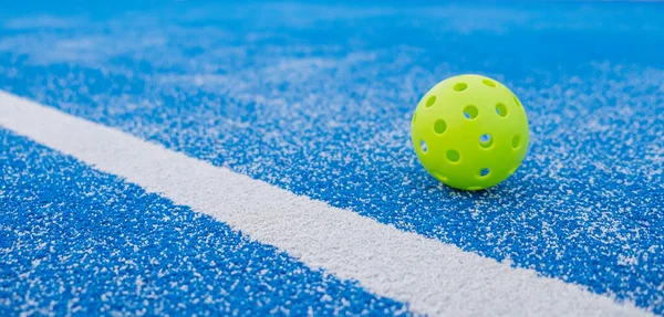 Pickleball topu mavi bir picleball sahasına yakın, afiş