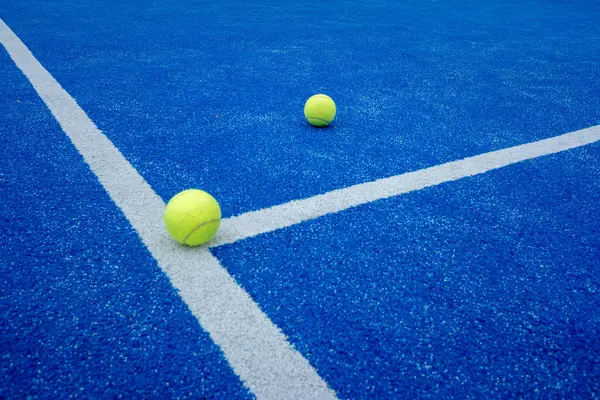 two paddle tennis balls over the line of a blue paddle tennis court