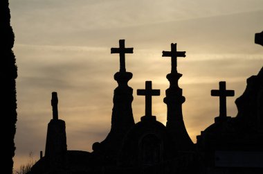 Gün batımında bir Hristiyan mezarlığında mezar silueti kesişiyor..