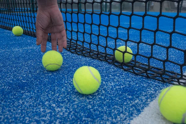 Hand of a man catching a ball next to the net of a blue paddle tennis court.