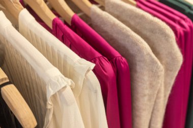 selective focus blouses and sweaters hanging from hangers in a clothing store clipart